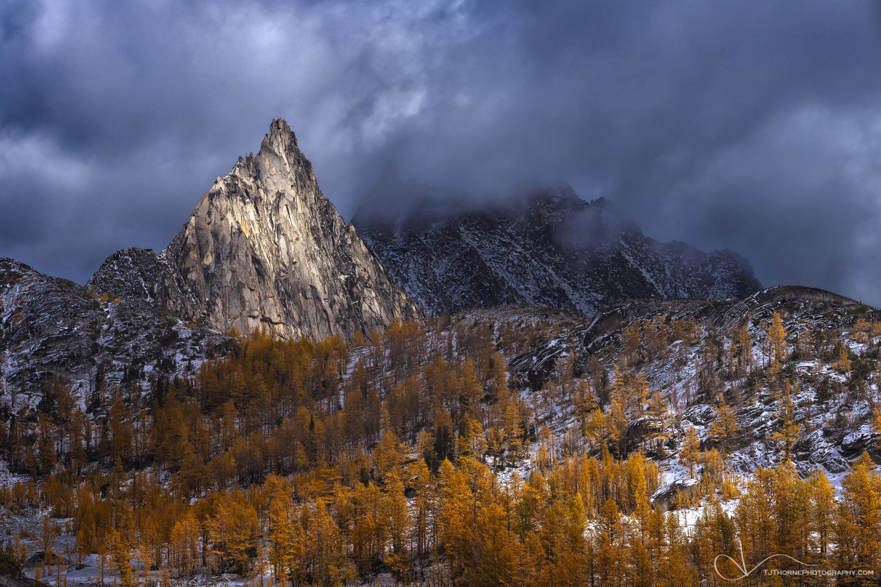 Mid-day light and shadows move across a grand scene of larch trees in their autumn dress and Prusik Peak in The Enchantments...
